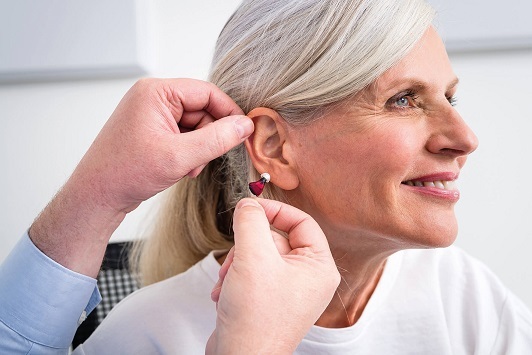 Ältere Frau bekommt ein modernes Hörgerät vom Hörakustiker ins Ohr eingesetzt.